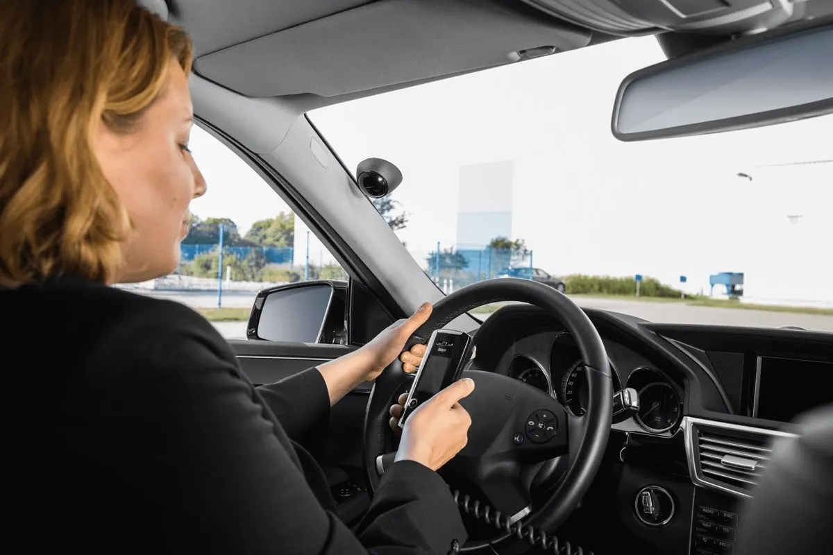 Driver taking a breath test while the ignition interlock camera above the windshield faces the driver seat.