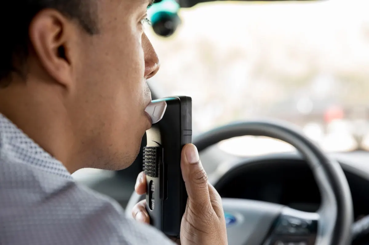 Driver blowing into a RoadGuard ignition interlock device before starting the car.