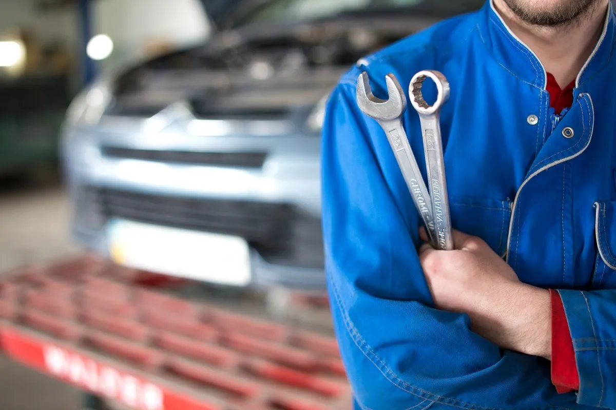 Service center technician who installs ignition interlock devices, holding two wrenches in the repair bay.