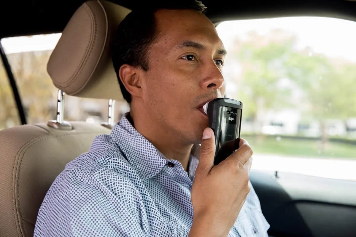 A driver gives a breath sample into a Dräger interlock handset for a rolling retest.